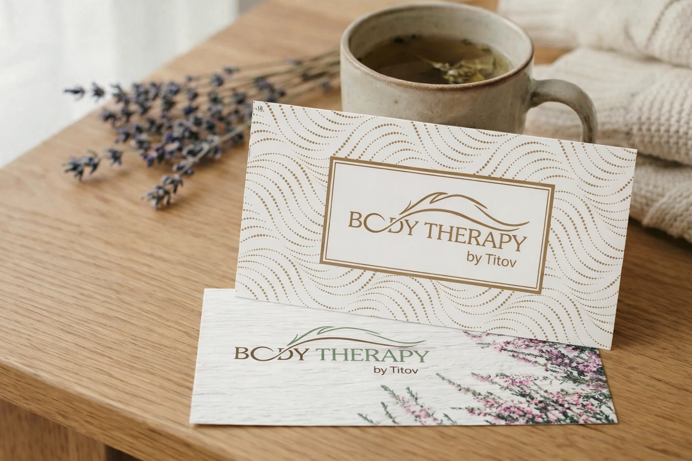 Therapy by Titov gift cards on a wooden table beside a cup of herbal tea and lavender, symbolizing a peaceful and harmonious wellness gift for all studio services.
