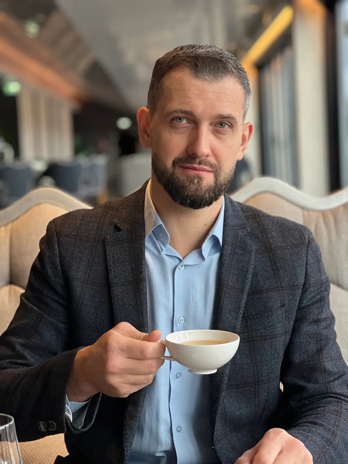 Coach and massage therapist Aleksejs Titovs from Therapy by Titov in a calm café setting in Riga with a cup of tea, reflecting the studio’s philosophy of thoughtful, balanced work with body, mind, and soul.