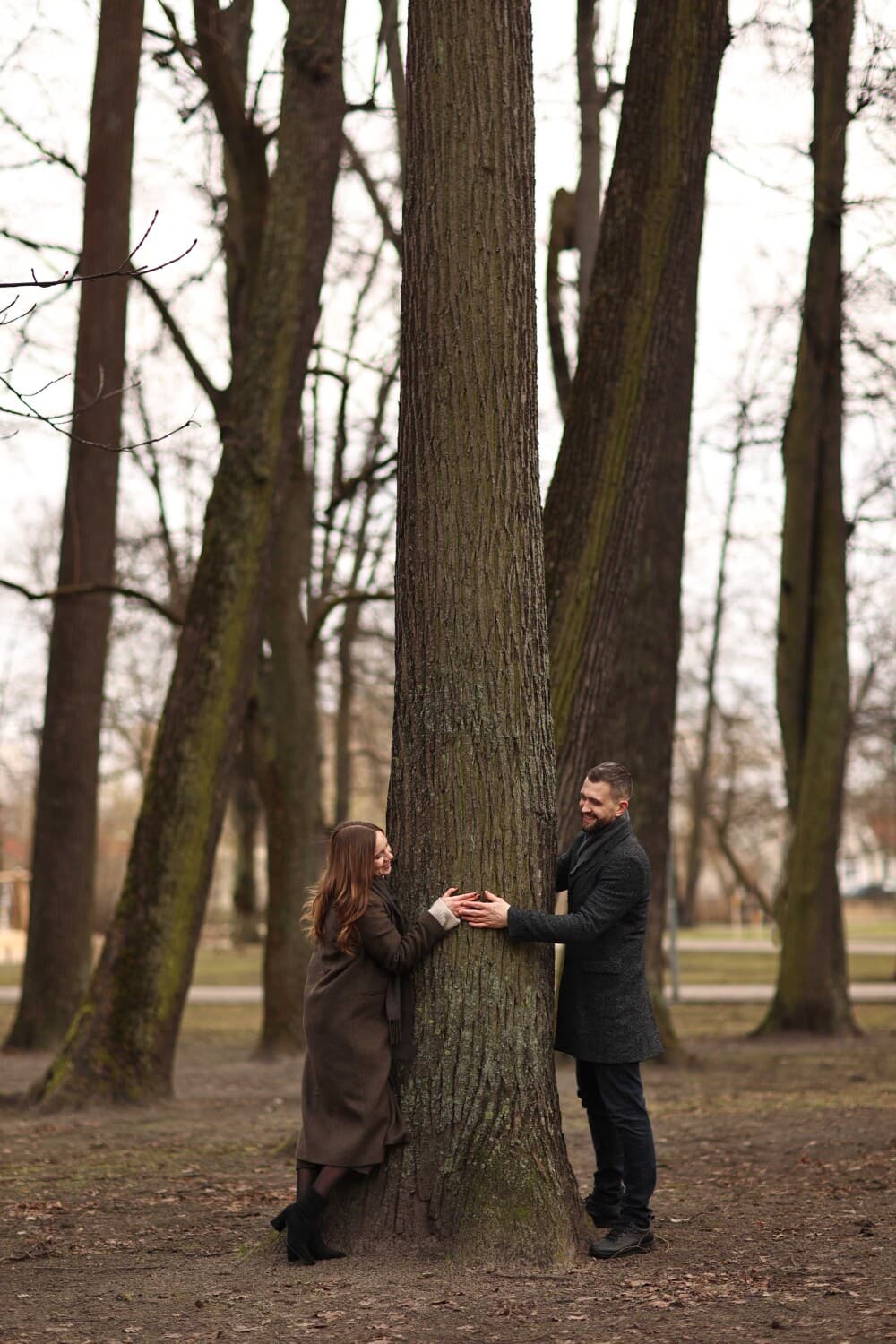 Aleksejs Titovs un Darja Titova in a Riga park resting their hands on a tree before a calming coaching and massage session.