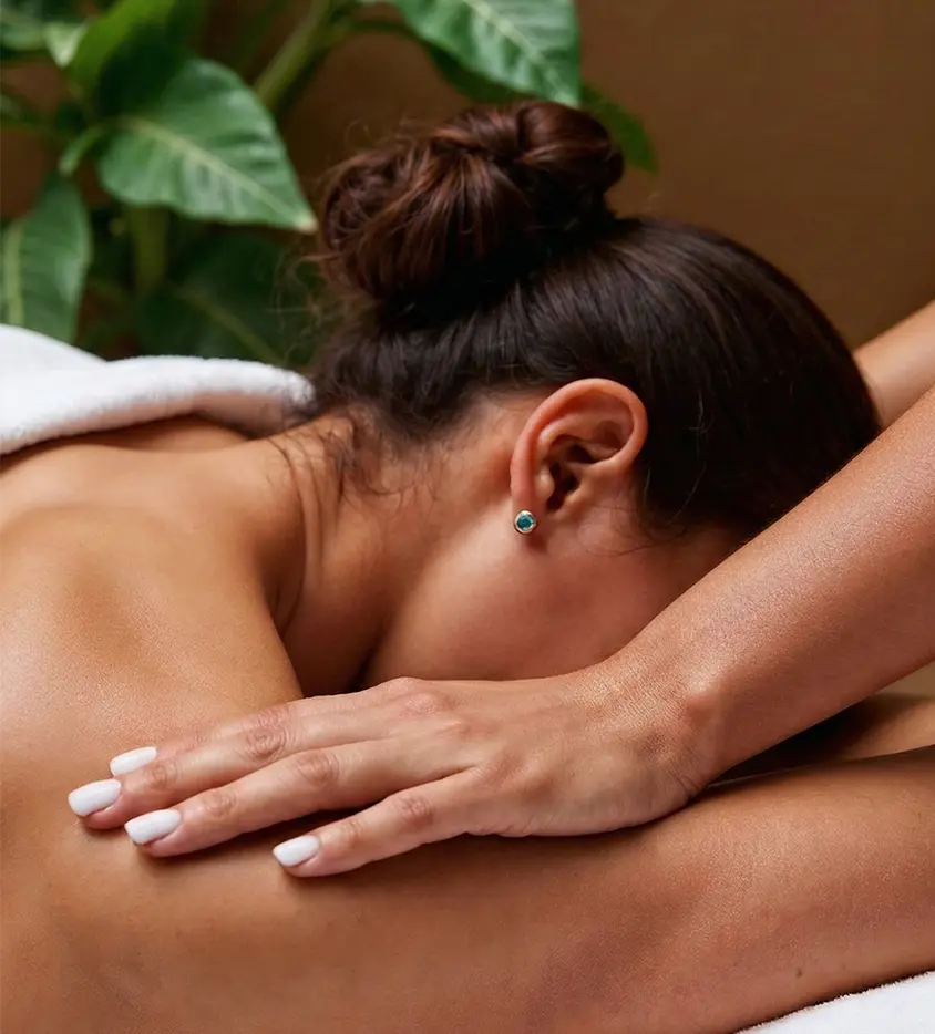 Full body massage for women with therapist Darja Titova from Therapy by Titov, working with her forearms along the client’s upper back, arms and neck and shoulder area in a calm room with green plants.
