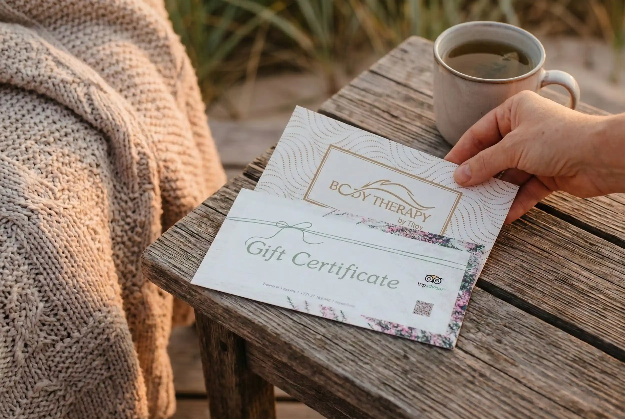 Therapy by Titov dāvanu kartes uz koka galda blakus lavandai, tasei zāļu tējas un mīkstam pledam.