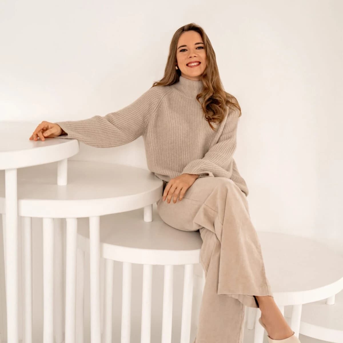 Therapy by Titov therapist Darja Titova sitting on white steps in a bright studio, symbolising unique, detail-oriented work with each person.