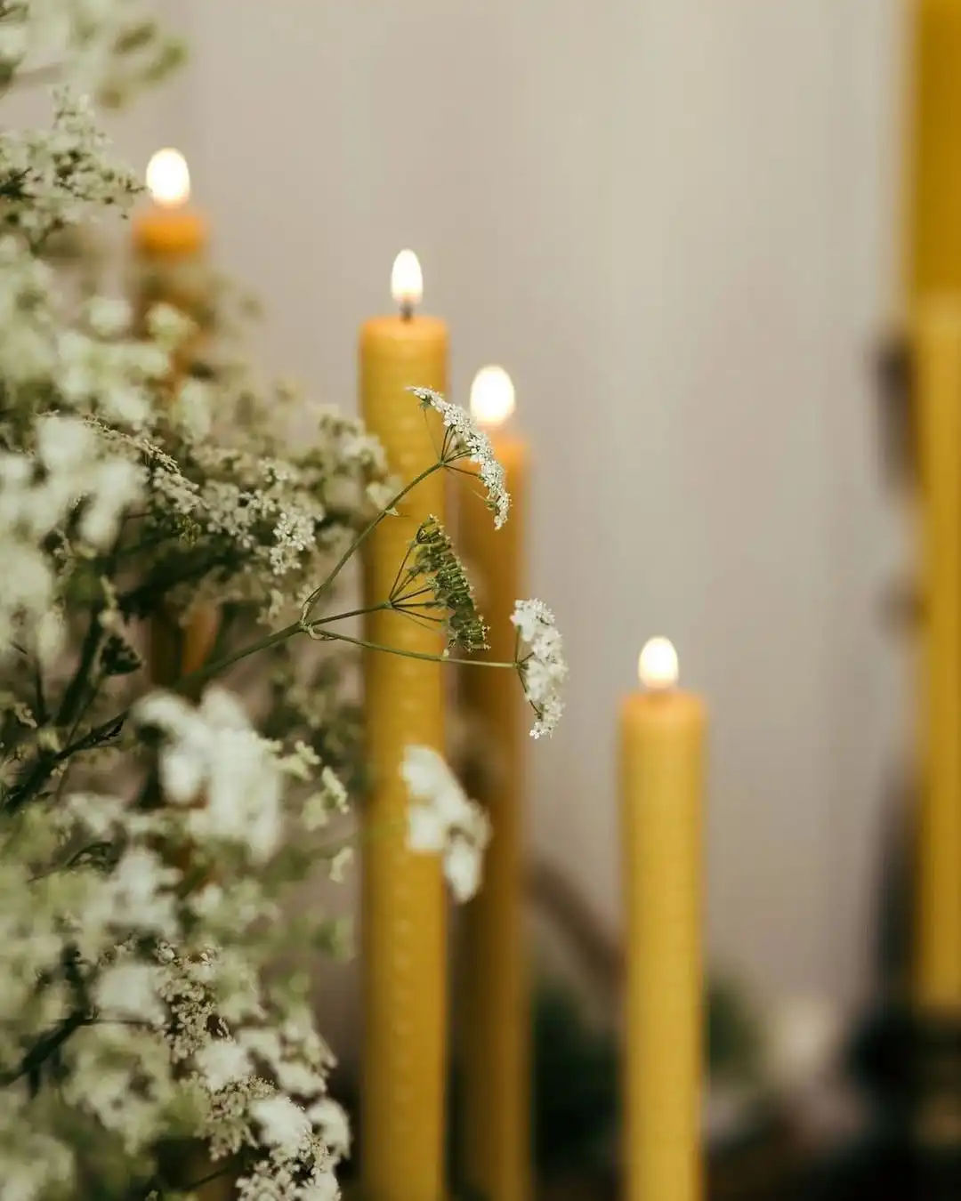 Garas bišu vaska sveces deg starp baltiem pļavas ziediem, veidojot maigu un mierpilnu enerģētiskās attīrīšanas altāri.