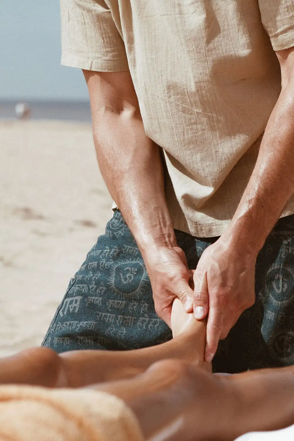 Therapy by Titov therapist Aleksejs Titovs on the beach gently working on a client’s foot, showing careful and safe massage.